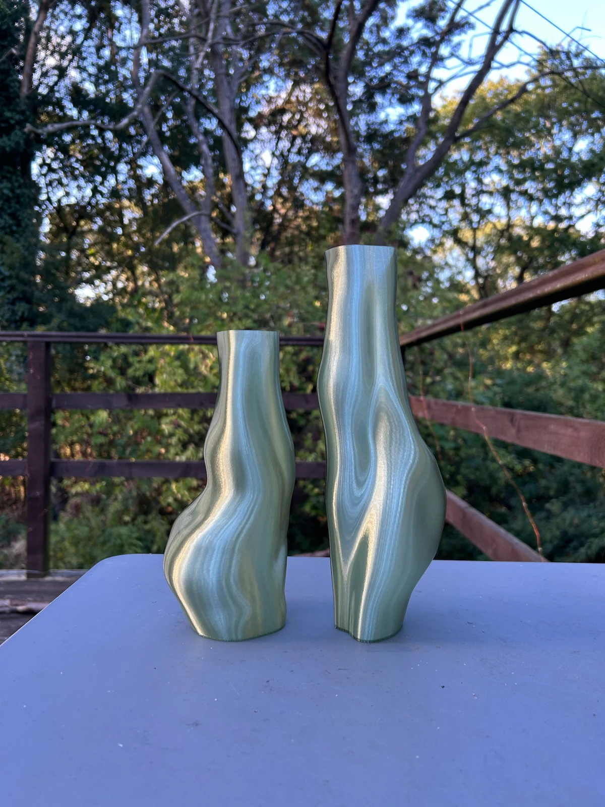 Two green sculptural vases, one tall and one short, with curves facing outward on a blue outdoor table
